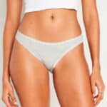 A woman’s midsection wearing a light gray lace-trimmed bikini-style underwear and a white cropped top, showcasing smooth, hair-free skin.