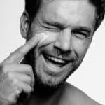 Laughing man applying lotion to his face
